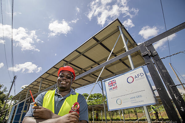 Kenianischer Arbeiter steht vor Solarmodul eines Mini-Grid