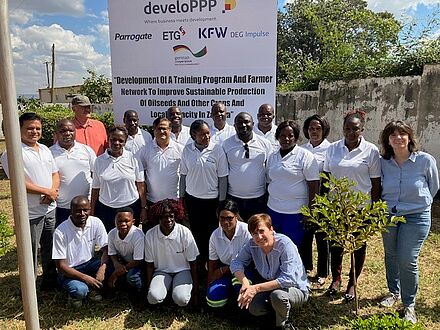 Absolventen und Absolventinnen eines landwirtschaftlichen Trainings in Sambia mit Kursleiter und Leiterin vor einer Infotafel, die das Programm benennt