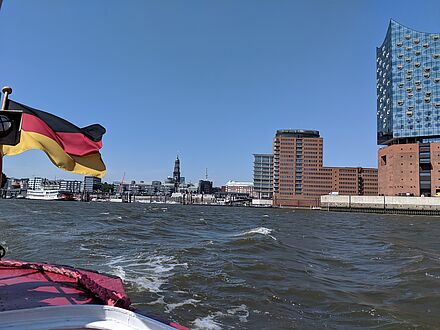 Foto der Elbphilharmonie mit Wasser im Vordergrund und einer Deutschland Flagge