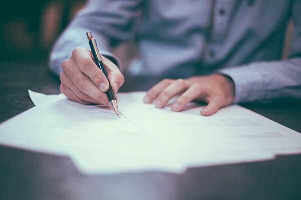 Männerhand mit Stift schreibt auf ein Blatt Papier