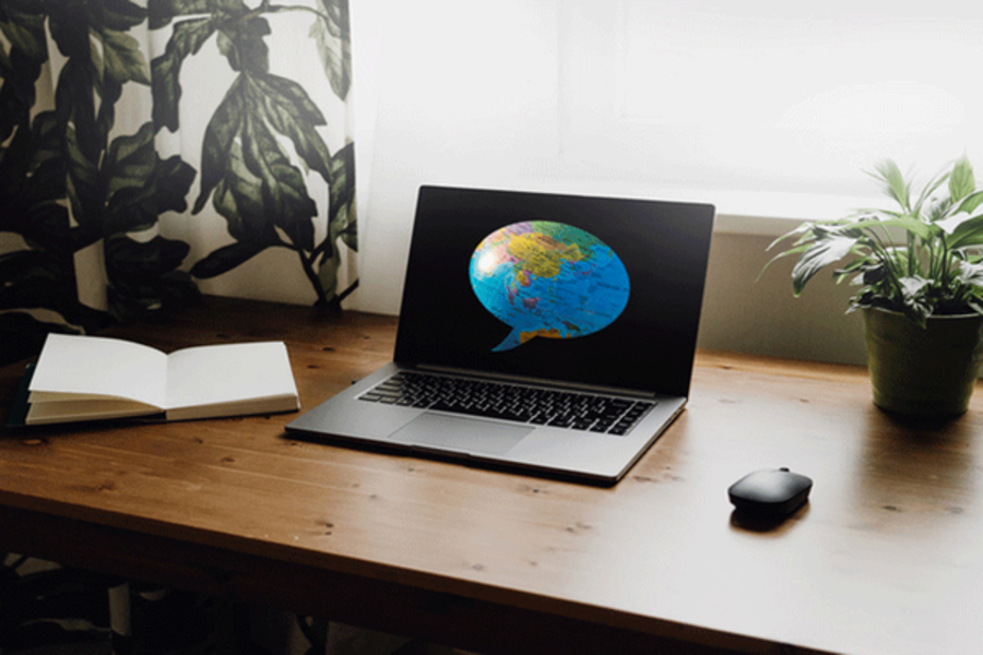 Ein Laptop steht auf einem hölzernen Schreibtisch, auf dem Bildschirm ist eine Weltkugel zu sehen
