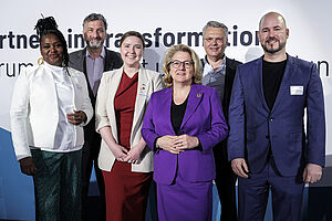 sechs Personen in Business-Kleidung gucken in die Kamera