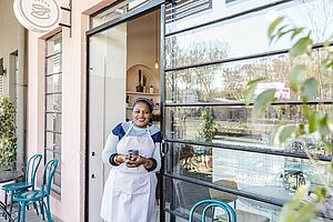 Latin shop keeper leaning at the door of her restaurant with glas facade