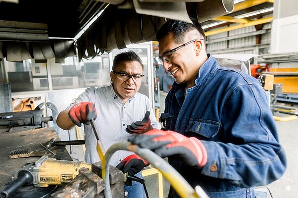 Auf dem Bild sieht man einen jungen Mann mit einem Ausbilder bei der Arbeit an einer Maschine. 