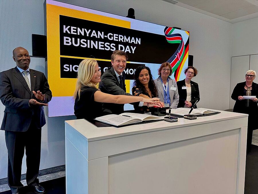 Mehrere Menschen legen ihre Hände aufeinander auf einen Knopf. Im Hintergrund steht auf einem Monitor "Kenyan-German Business Day".