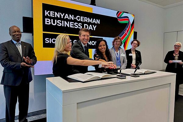 Mehrere Menschen legen ihre H&auml;nde aufeinander auf einen Knopf. Im Hintergrund steht auf einem Monitor "Kenyan-German Business Day".