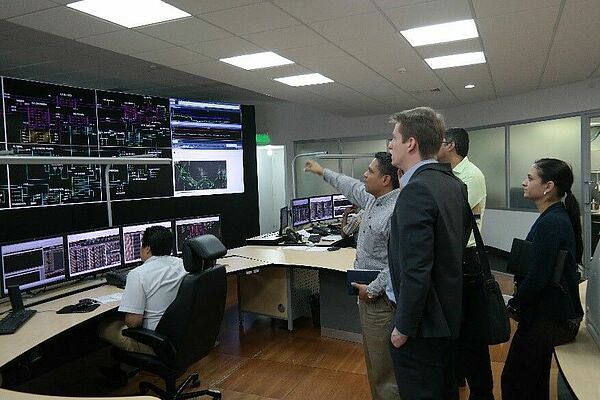 Mehrere Menschen schauen auf große Monitore in einem Büroraum mit künstlichem Licht.
