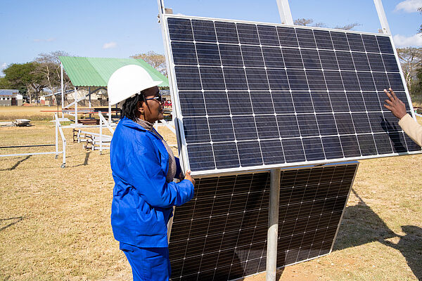Eine Facharbeiterin mit einem wei&szlig;en Helm steht neben einem Solar-Panel.